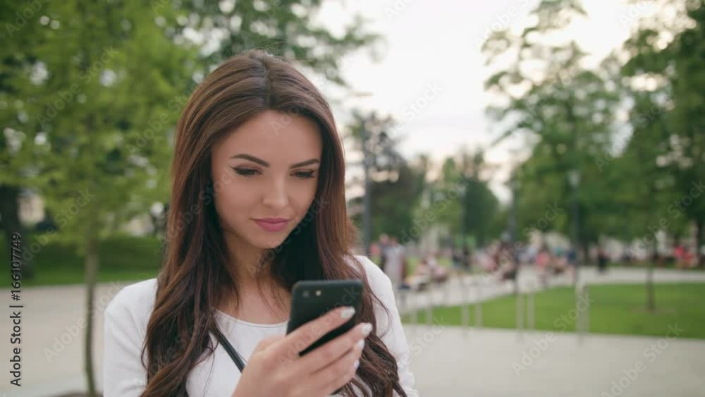 A beautiful brunette young lady using a smapthone outdoors. Soft focus. Dolly shoot A beautiful brunette young lady using a smapthone outdoors. Soft focus. Dolly shoot