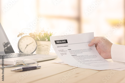 Businessman review his resume on his wooden desk before sending to find a job with laptop computer.
