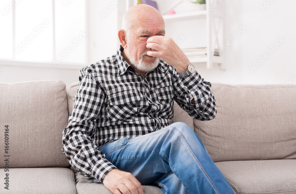 Elderly man with headache pinching back of nose Elderly man with headache pinching back of nose