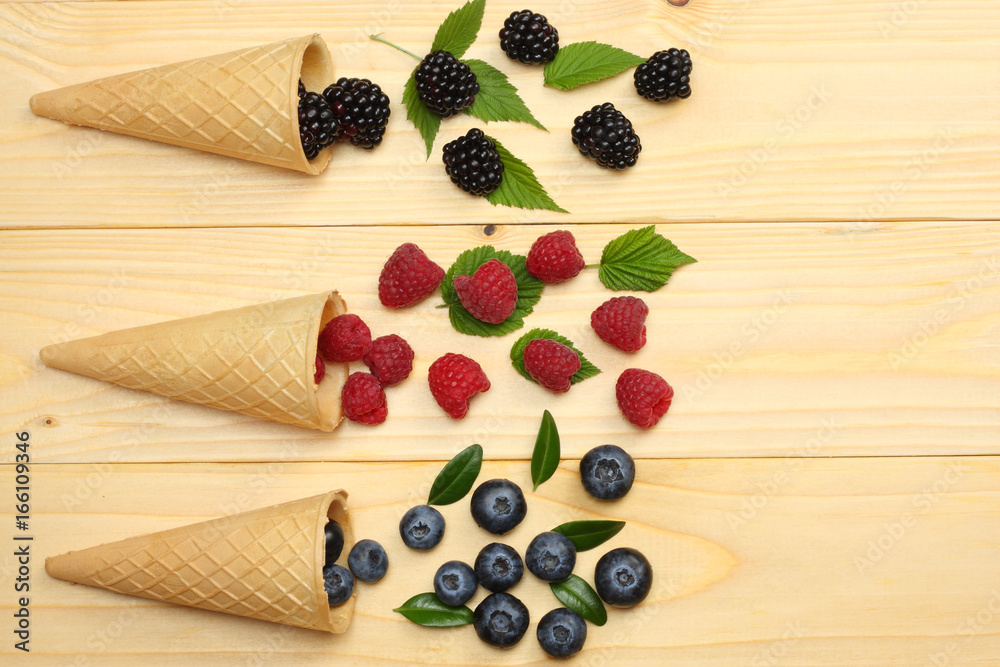 mix of blueberries, blackberries, raspberries in ice cream cone on light wooden table background. top view with copy space mix of blueberries, blackberries, raspberries in ice cream cone on light wooden table background. top view with copy space