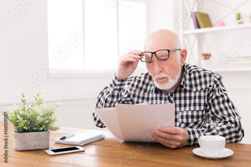 Shocked senior man looking at bills copy space