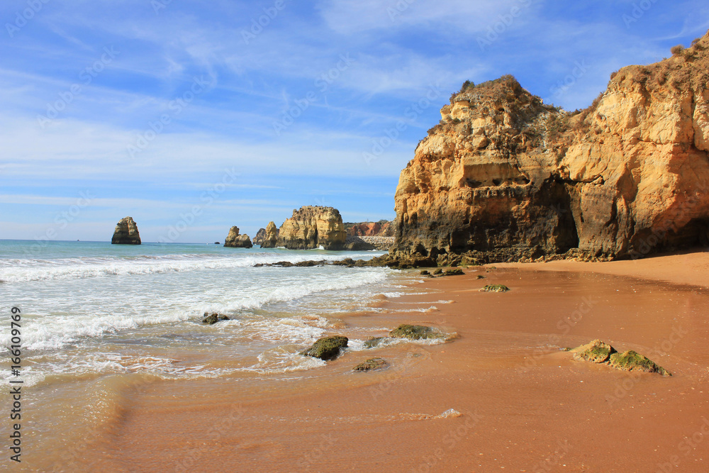 Scenic hidden beach shore cliff rocks, sand waves, sunny summer day with no people. Algarve region in Portugal ocean water coast line outdoor landscape. Travel tourism vacation trip concept background