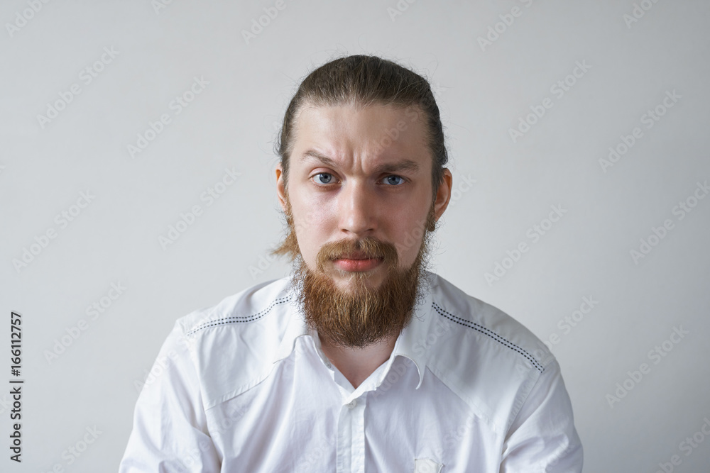 Headshot of displeased angry unshaven young employee staring at camera with grumpy and pissed off look, frowning, having bad mood, feeling dissatisfied and furious about something. Human emotions