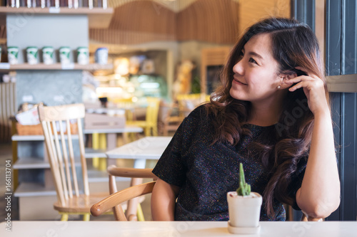 Closeup portrait image of a smiley beautiful Asian woman with feeling good sitting and relaxing in cafe with a small cactus pot on wooden table © Farknot Architect