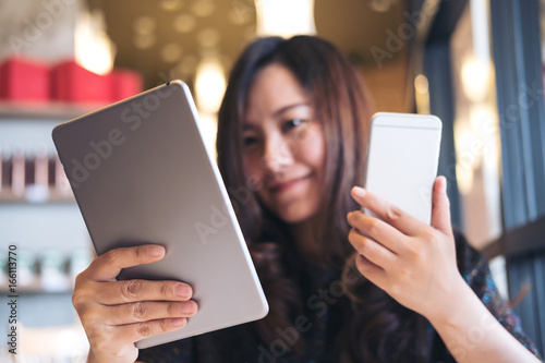 A beautiful Asian business woman holding tablet pc and smart phone while working in modern cafe