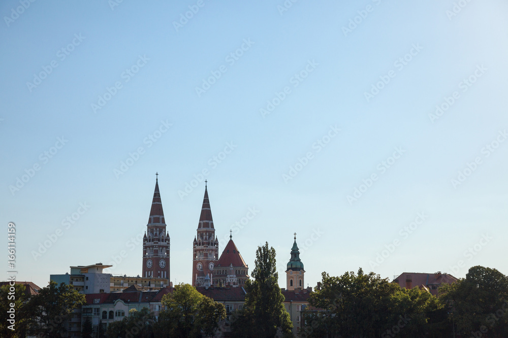 Szeged city center, with a highlight on Szeged Cathedral, seen into the light during sunset in summer.