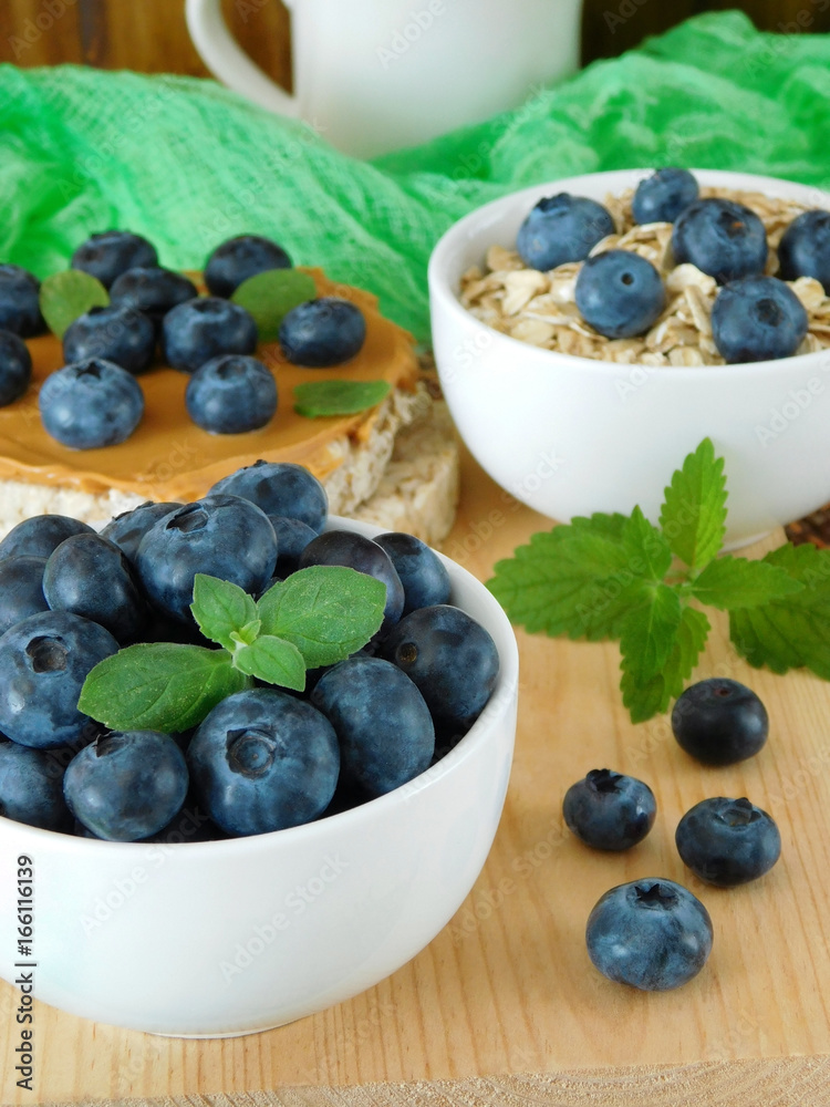 Blueberries in a ceramic bowl. Oatmeal and sandwich with peanut butter in the background Blueberries in a ceramic bowl. Oatmeal and sandwich with peanut butter in the background