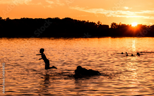 Kids and families are having fun at a lake under sunset
