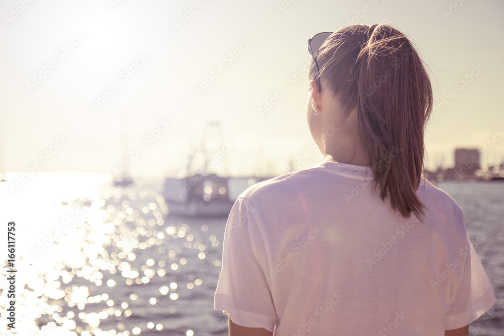 The young girl looks at the sea with her back facing The young girl looks at the sea with her back facing