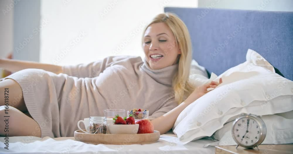 Beautiful woman eating breakfast with yogurt, fruit and cereals on bed. Morning wake up at home in bedroom. Caucasian people liying on bed. 4k video Beautiful woman eating breakfast with yogurt, fruit and cereals on bed. Morning wake up at home in bedroom. Caucasian people liying on bed. 4k video