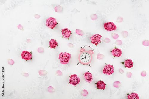 Pink rose flowers, petals and alarm clock on white desk from above in flat lay style. Wake up concept.