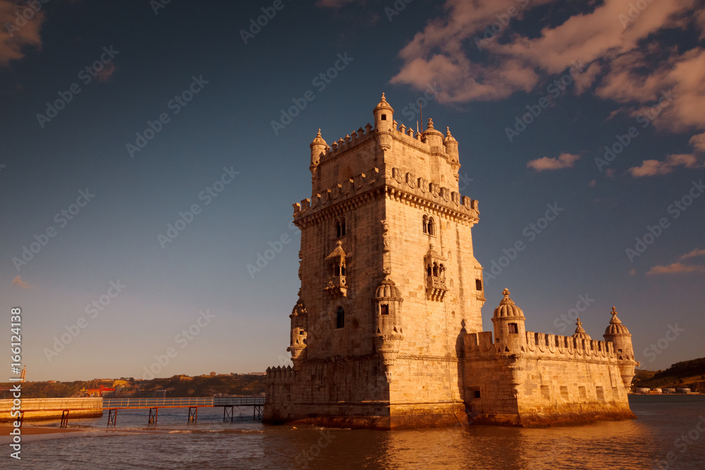 A golden hour wide angle shot of the Torre de Belem tower, Lisbon, Portugal, against a blue sky with volumetric clouds