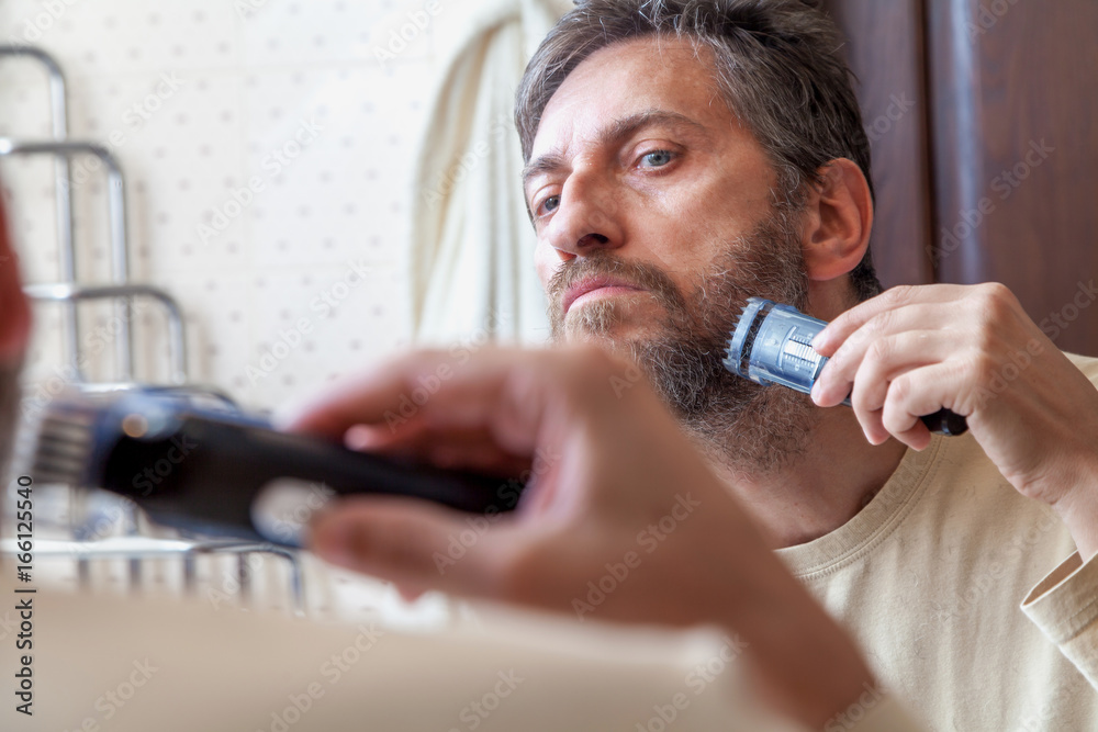 Grooming beard. Man alone shears beard in bathroom Grooming beard. Man alone shears beard in bathroom