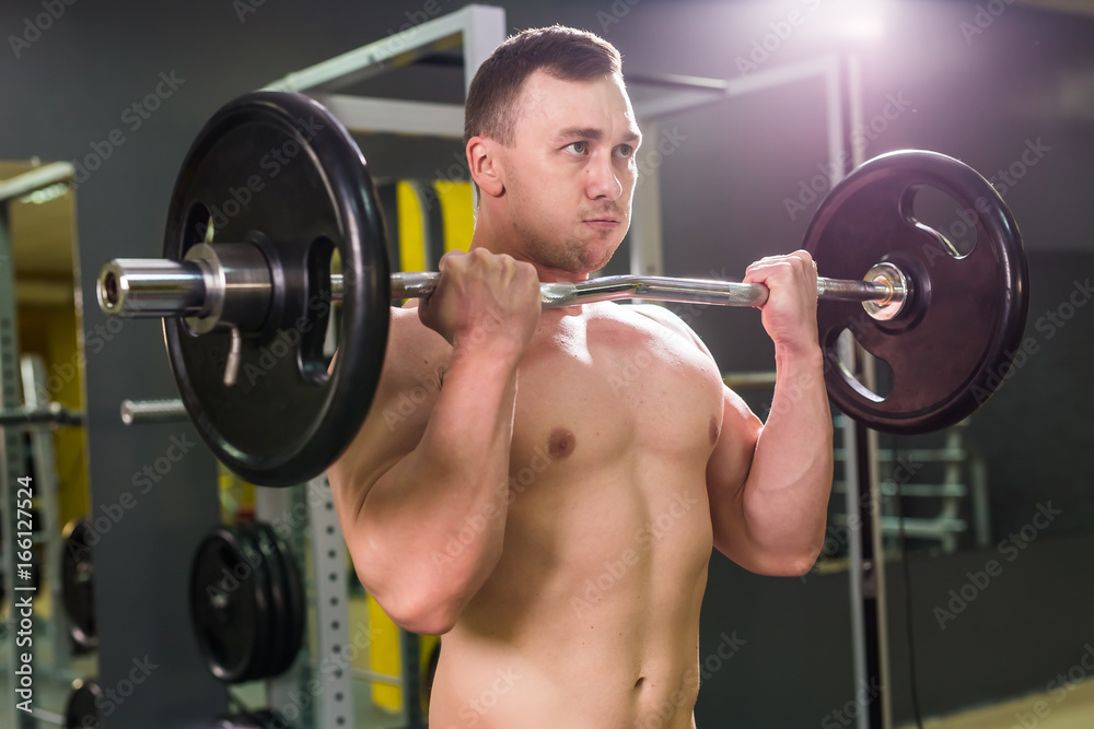 Strong man - bodybuilder with dumbbells in a gym, exercising with a barbell. Strong man - bodybuilder with dumbbells in a gym, exercising with a barbell.