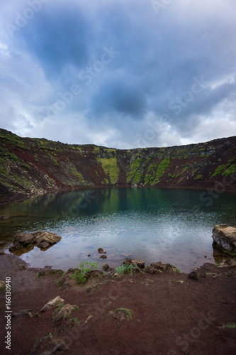 Iceland - Red dusty ground before clear blue water at Kerid Crater Lake