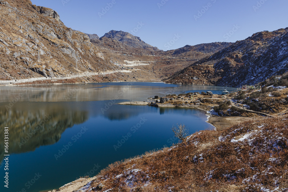 Frozen pond with ice on the frozen surface with brown mountain and clear sky in the background in winter in Tashi Delek near Gangtok. North Sikkim, India