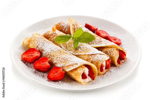 Crepes with strawberries and cream on white background