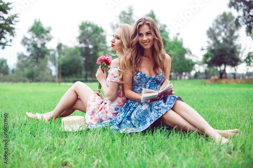 Wallpaper Mural Best friends women having fun in park. Two beautiful young women sit back to back on the lawn in the park. Torontodigital.ca