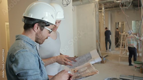 Among the repairs, two men in helmets discuss a project on securities. The construction team works for the reconstruction of the premises. People around color, clean and clean. A tall customer with a