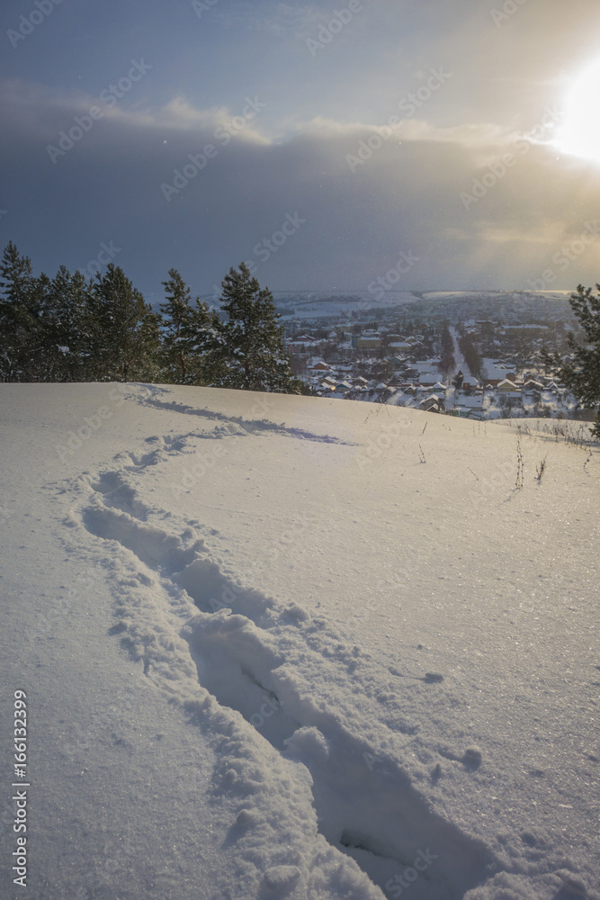 Human footprints in the snow lead to the hillside town in the background