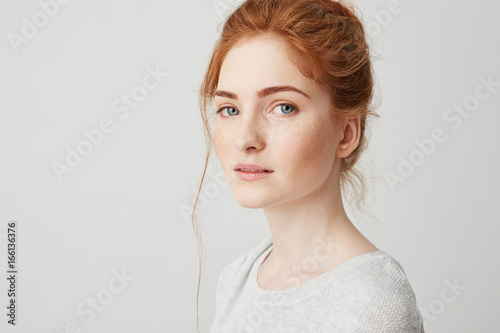 Close up of young tender beautiful ginger girl with blue eyes looking at camera over white background. Copy space.
