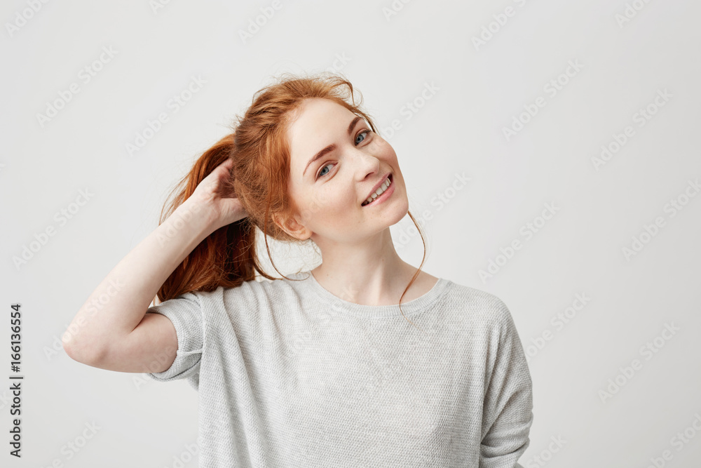 Portrait of young cute redhead girl smiling looking at camera touching hair over white background. Portrait of young cute redhead girl smiling looking at camera touching hair over white background.