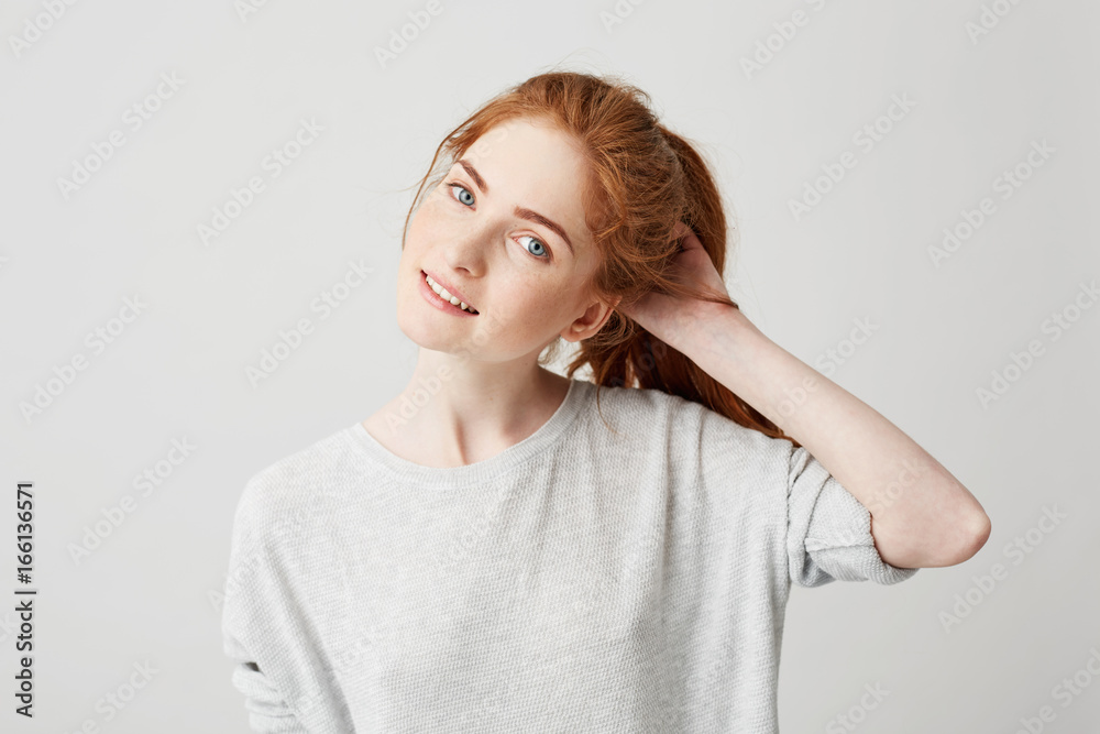 Portrait of young cute redhead girl smiling looking at camera touching hair over white background. Portrait of young cute redhead girl smiling looking at camera touching hair over white background.