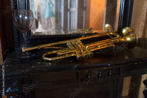 Gold trumpet laying on a table with a glass of wine and young lady reflection in the mirror
