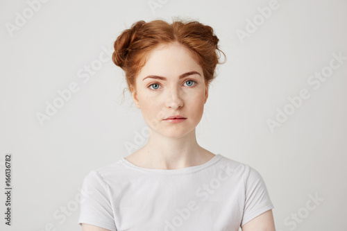 Close up photo of young beautiful ginger girl with buns looking at camera over white background.