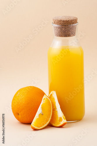 Fresh orange juice in a glass bottle and orange on a light beige background..