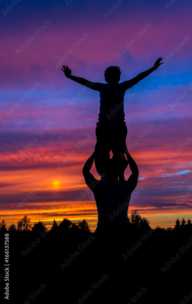 Boy standing on the father shoulders silhouette with colorful sunset