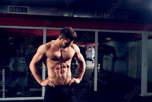 Handsome bodybuilder is standing in the modern gym.