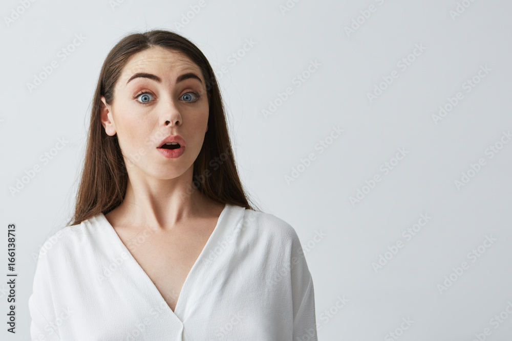 Fototapeta premium Portrait of surprised young beautiful businesswoman looking at camera with opened mouth over white background.