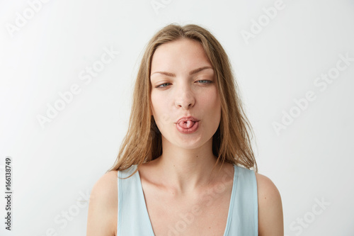 Portrait of funny cheerful young girl showing tongue over white background.