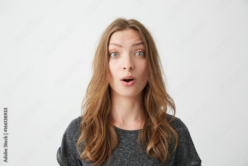 Portrait of surprised young beautiful girl with opened mouth looking at camera over white background.