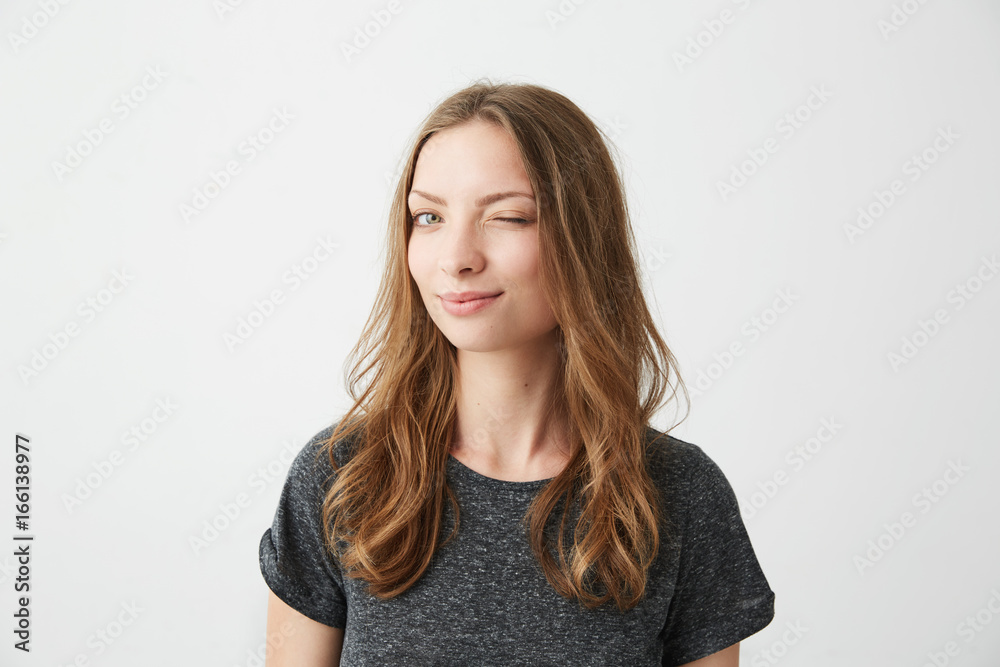 Obraz premium Portrait of young positive girl smiling winking looking at camera over white background.