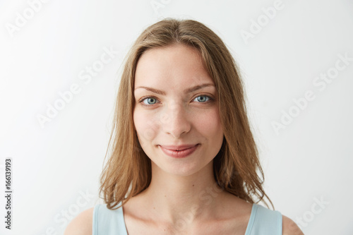 Close up portrait of young beautiful blonde girl with blue eyes smiling looking at camera over white background.