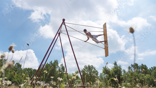 Boy teenager high riding on a swing, against the sky