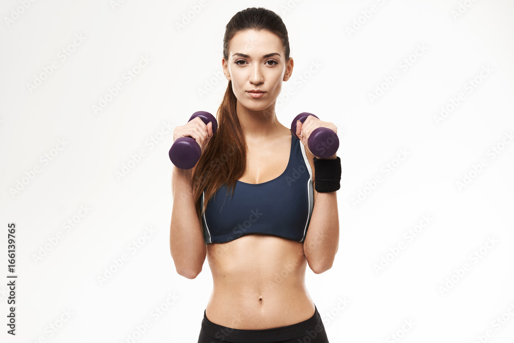 Sportive beautiful girl with dumbbells in sportswear posing looking at camera over white background. Sportive beautiful girl with dumbbells in sportswear posing looking at camera over white background.