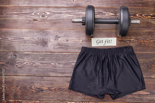 Sport equipment for muscle training. Athletic shorts and barbell, wooden background. Sport as lifestyle. photo