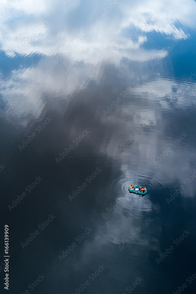 Aerial view of the lake with fishing boat and reflecting clouds 