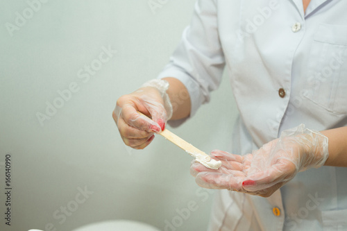 Hands of the beautician in gloves, diluted cream face mask in the salon