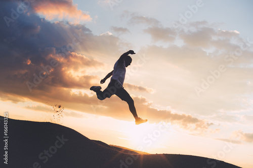 Silhouette of an extreme sportsman engaged in outdoor sports at sunset. Athlete jumping over the ravine. Intentional dark colors