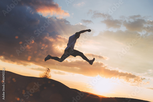 Silhouette of extreme man running over the hills at beautiful sunset. Intentional dark colors