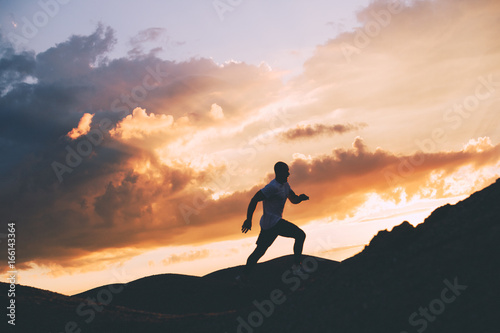 Silhouette of a strong runner on background of beautiful sunset on outdoor. Fitness training. Jogging in nature. Intentional dark colors