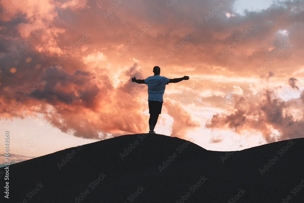 Happy male athlete  with hands up standing on hill at sunset