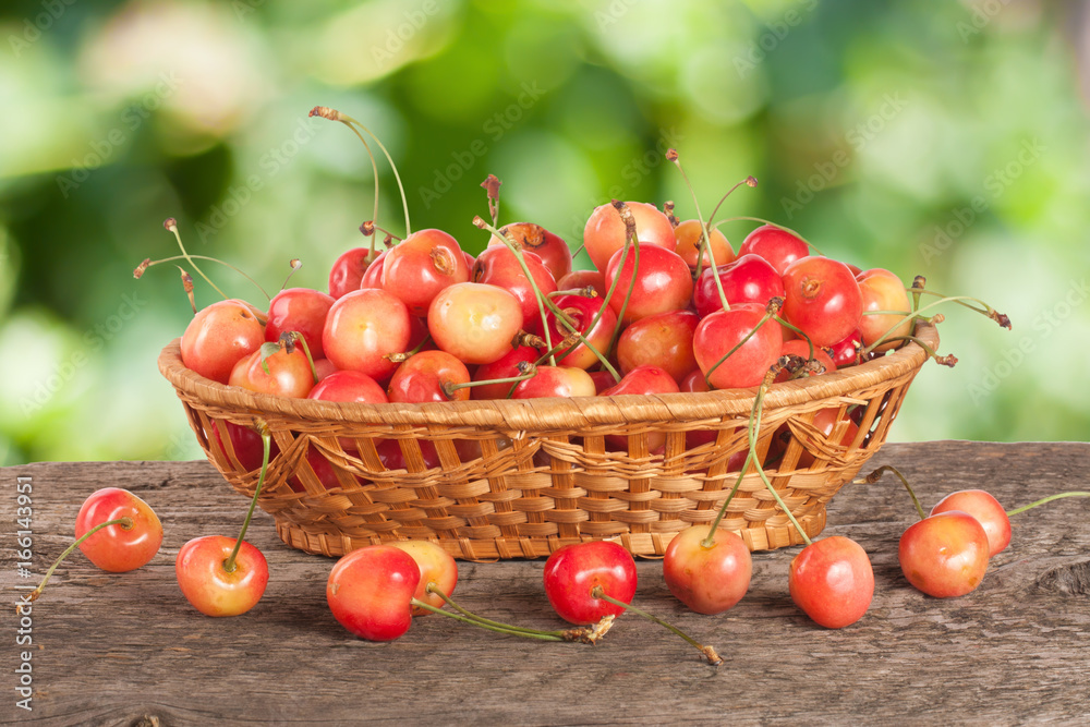 Yellow cherry in a wicker basket on a wooden table with a blurry garden background Yellow cherry in a wicker basket on a wooden table with a blurry garden background