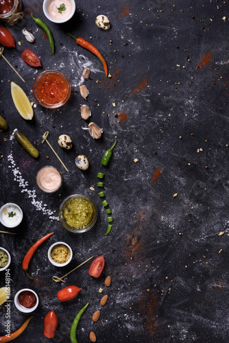 Variety of sauces, ingredients and snacks on dark messy table.