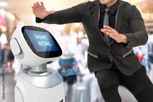 Smart retail sales and crm robot assistant or adviser technology concept. Man suit using robo-advisor display text on screen with blur shopping fashion mall background. photo