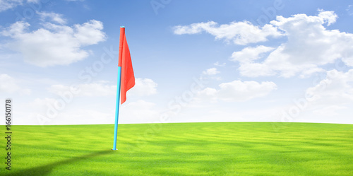 Flag on golf course with green grass and blue sky.